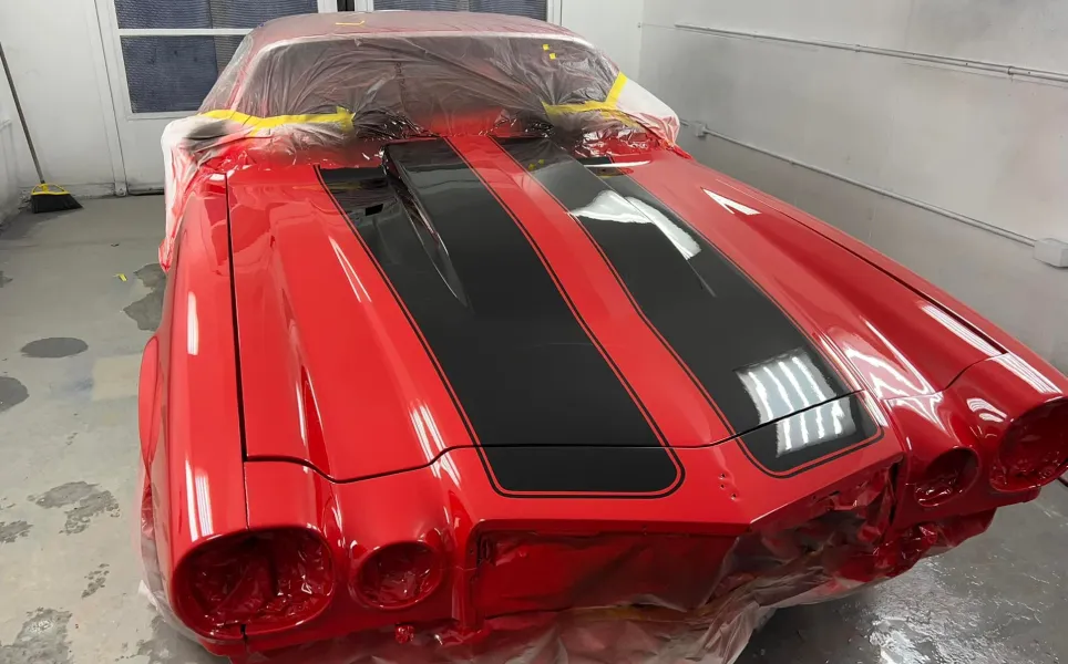 A red Camaro shell undergoing restoration and precision painting in the paint booth at Nathan’s Body Shop & Wrecker Service in Franklin, NC.