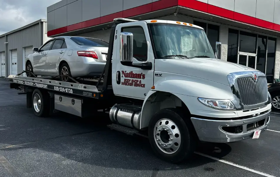 Car towing on a flatbed tow truck in a commercial parking lot.