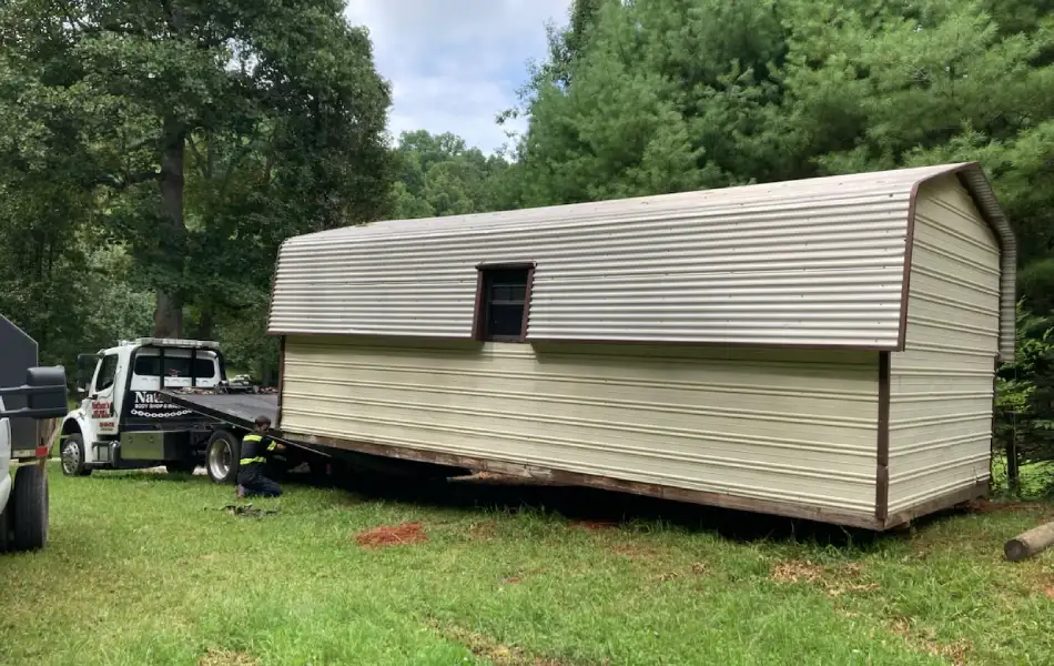 Tiny home towing on a flatbed tow truck in a grassy area.