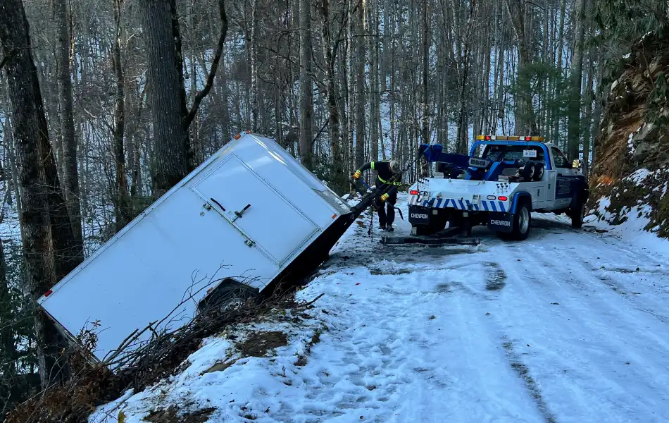 Trailer towing and recovery on a snowy mountain road.